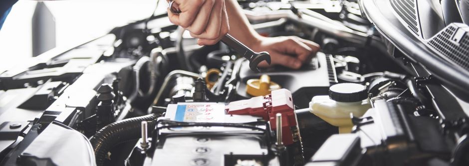 mechanic under the hood of a car and holding a spanner 