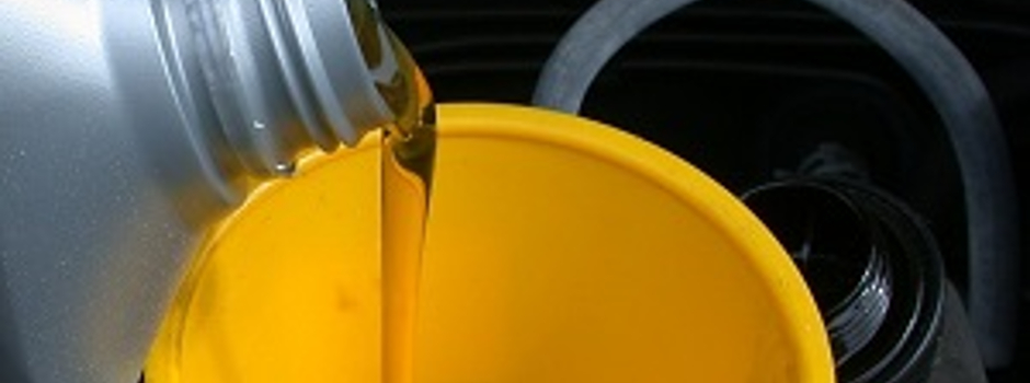 Engine oil in grey bottle being poured into car using a yellow funnel